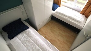 A small, compact room with a single bed, a window with curtains, and a wooden floor. - Comfort Vikingpark 40 (Westkapelle)