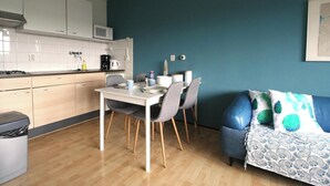 A compact kitchen with white cabinets, a microwave, and a coffee maker. There is a dining table with chairs and a blue sofa with patterned cushions. - Comfort Vikingpark 40 (Westkapelle)