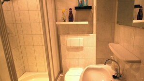 A bathroom with a shower, toilet, sink, and shelves with toiletries. - Comfort Vikingpark 40 (Westkapelle)