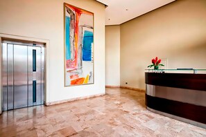 A modern lobby with a reception desk, a large abstract painting, and a metallic elevator.