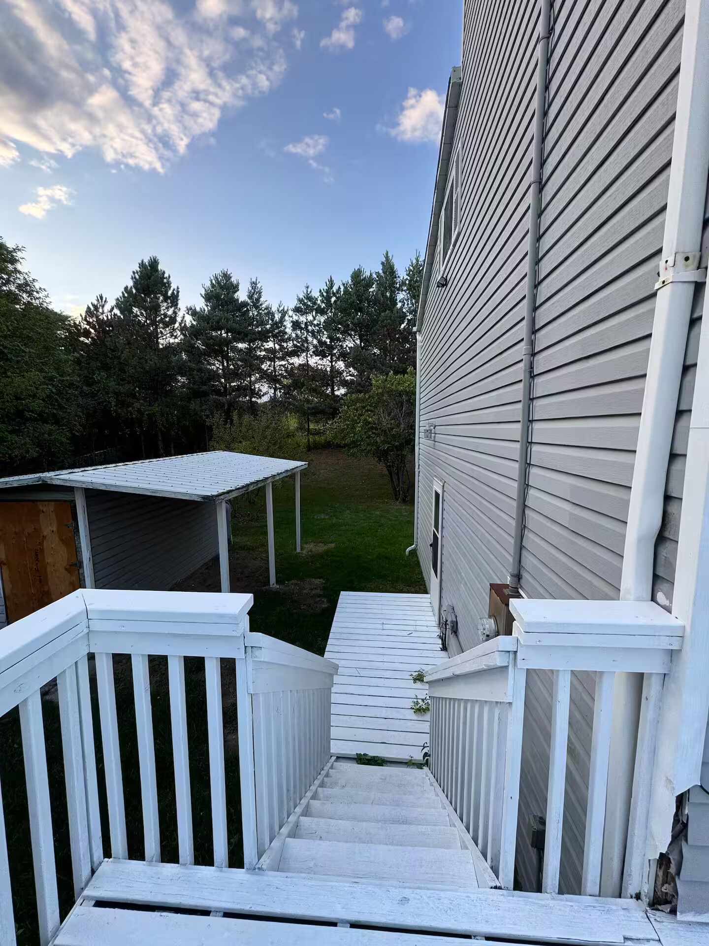 A wooden deck leading to a house with a covered porch and a small shed.