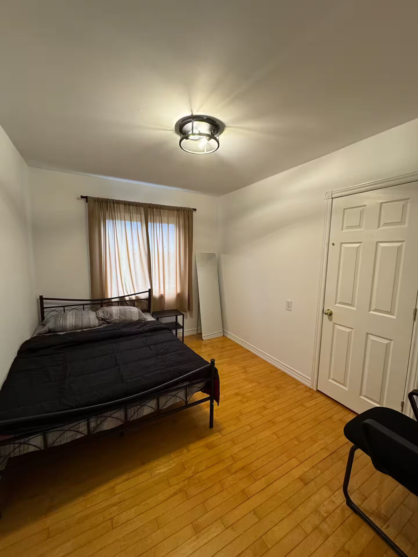 Une chambre à coucher avec un lit, une chaise, une porte et une fenêtre avec des rideaux.