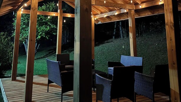 An outdoor wooden deck with chairs and tables, under a wooden pergola with string lights. - Cozy getaway in Brighton (Brighton)