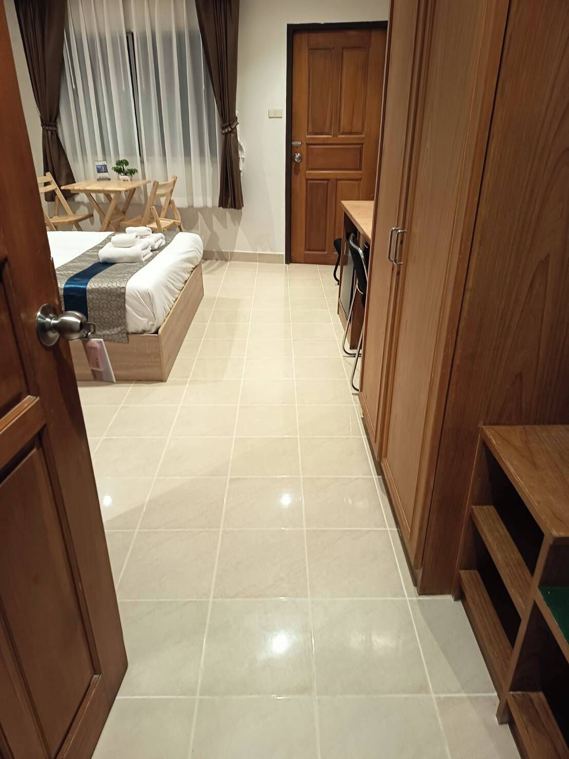 A hotel room with a bed, a desk, and a chair. There is a door leading to another room.