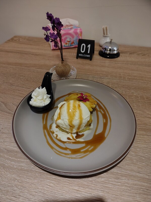 Ein Desserteller mit einer Kugel Eis und Karamellsauce, eine kleine Schale Schlagsahne und eine Zierblume auf einem Holztisch.
