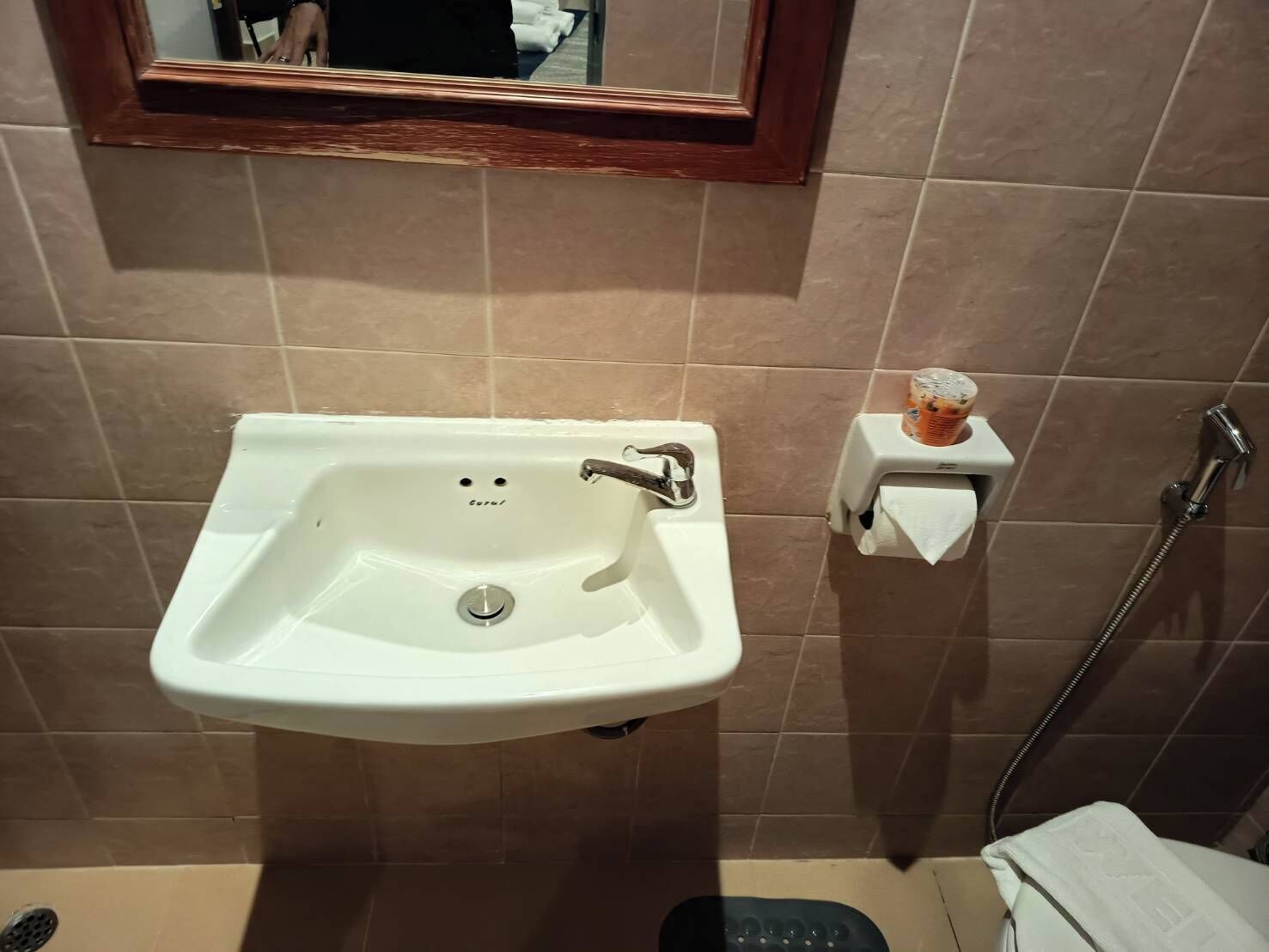 Un baño con un lavamanos blanco, un espejo encima, un dispensador de toallas y una zona de ducha.