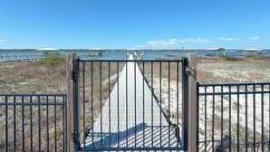 Une promenade en bois mène à une plage d’où l’on a une vue dégagée sur l’eau et sur des bâtiments situés au loin.