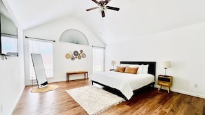 A bedroom with a bed, a ceiling fan, a bedside table with a lamp, a bench, and a mirror. - Big Backyard w/pool, Centrally Located (The Colony)