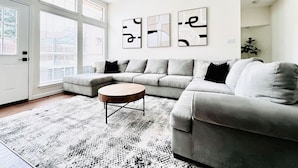 A modern living room with a grey sectional sofa, a round coffee table, and abstract wall art. - Big Backyard w/pool, Centrally Located (The Colony)