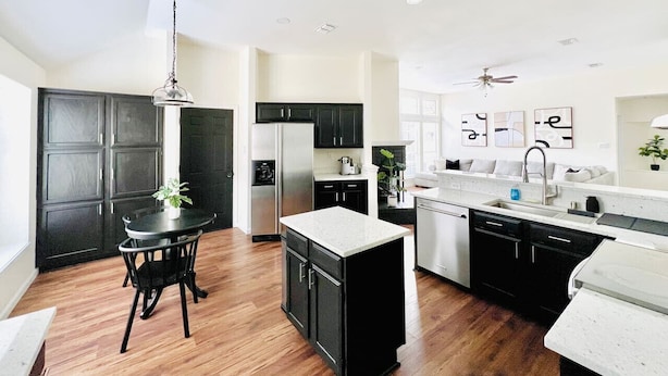 A modern kitchen with a central island, black cabinets, and a dining area with a table and chairs. - Big Backyard w/pool, Centrally Located (The Colony)