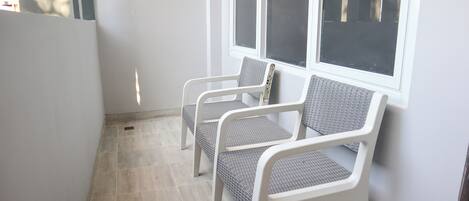 A corner with two white chairs with mesh backs, a tiled floor, and a window with blinds.