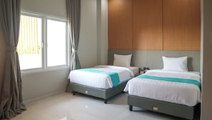 Ein Hotelzimmer mit zwei Betten, einem Holzkopfende und einem großen Fenster mit Vorhängen.