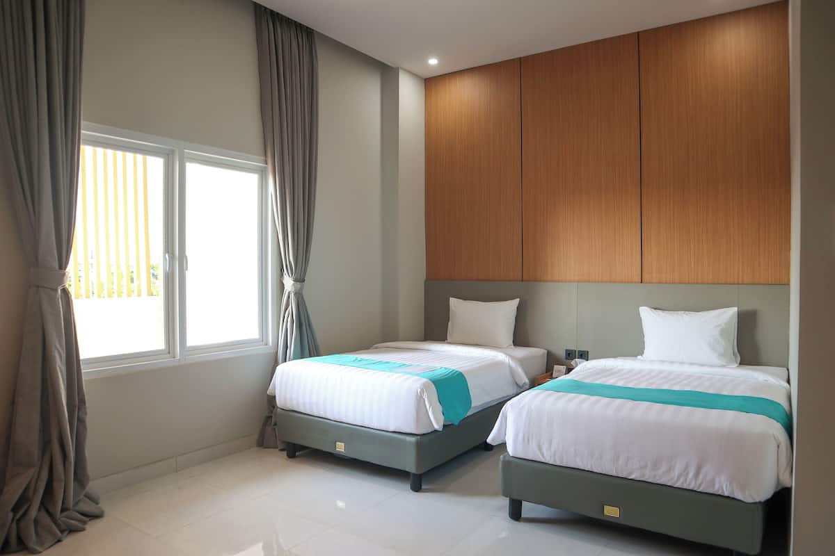 A hotel room with two beds, a wooden headboard, and a large window with curtains.
