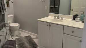 A bathroom with a white sink, mirror, and toilet. There are two rugs on the floor and a towel rack with towels.