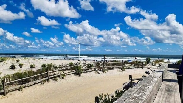A beach view with a wooden fence, sandy beach, and ocean in the background. - The Breakaway Beach Condo (North Wildwood)