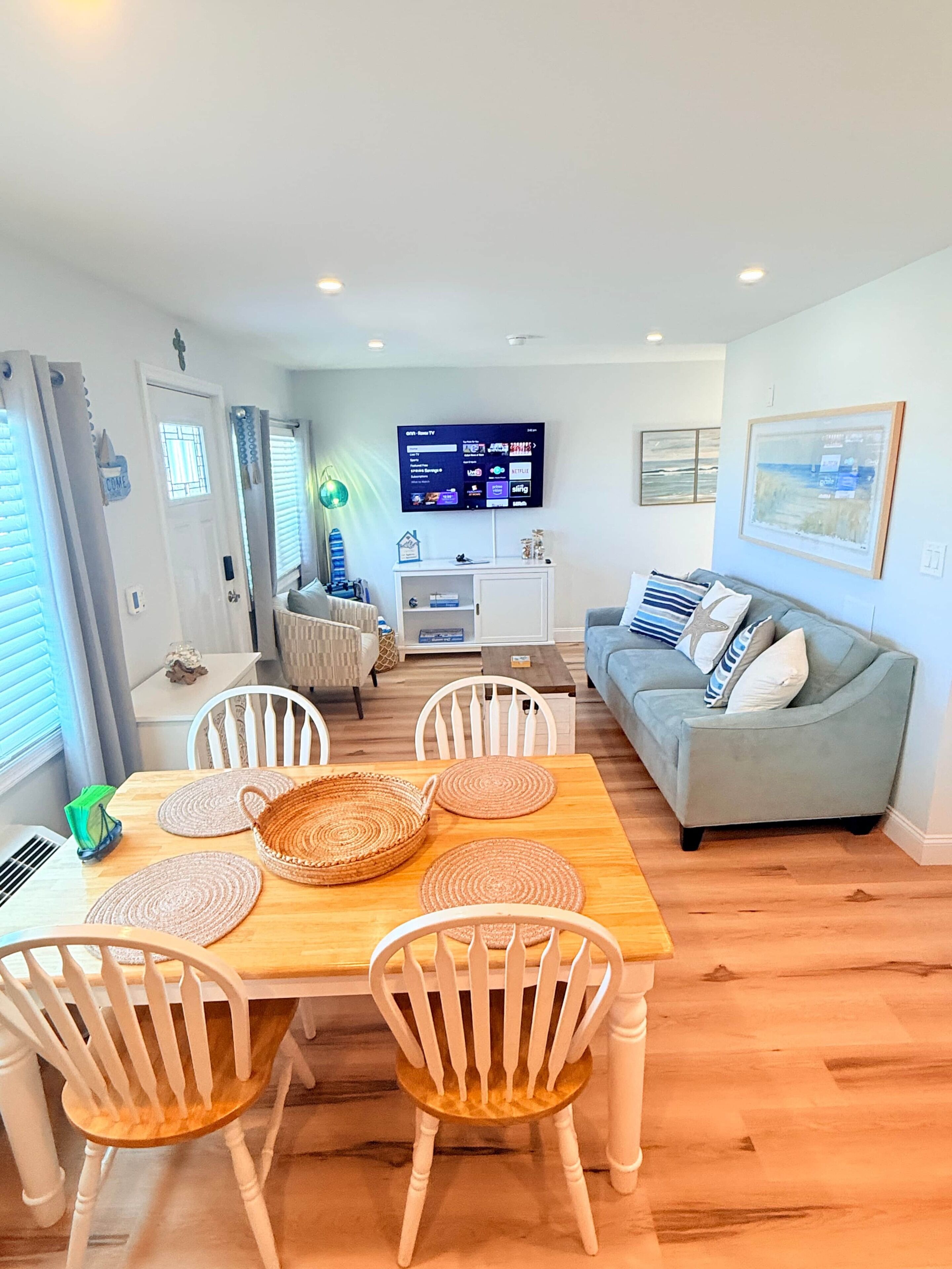 A modern living room with a dining area, a grey sofa, and a flat-screen TV mounted on the wall.