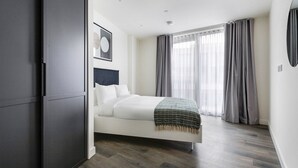 Une chambre moderne avec un lit, une armoire sombre et une grande fenêtre avec des rideaux.