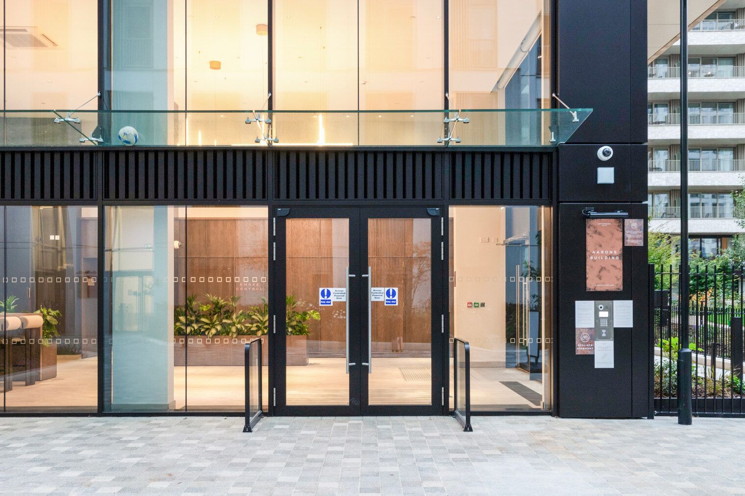 A modern building entrance with glass doors, a metal barrier, and a sign indicating a wheelchair-accessible entrance.
