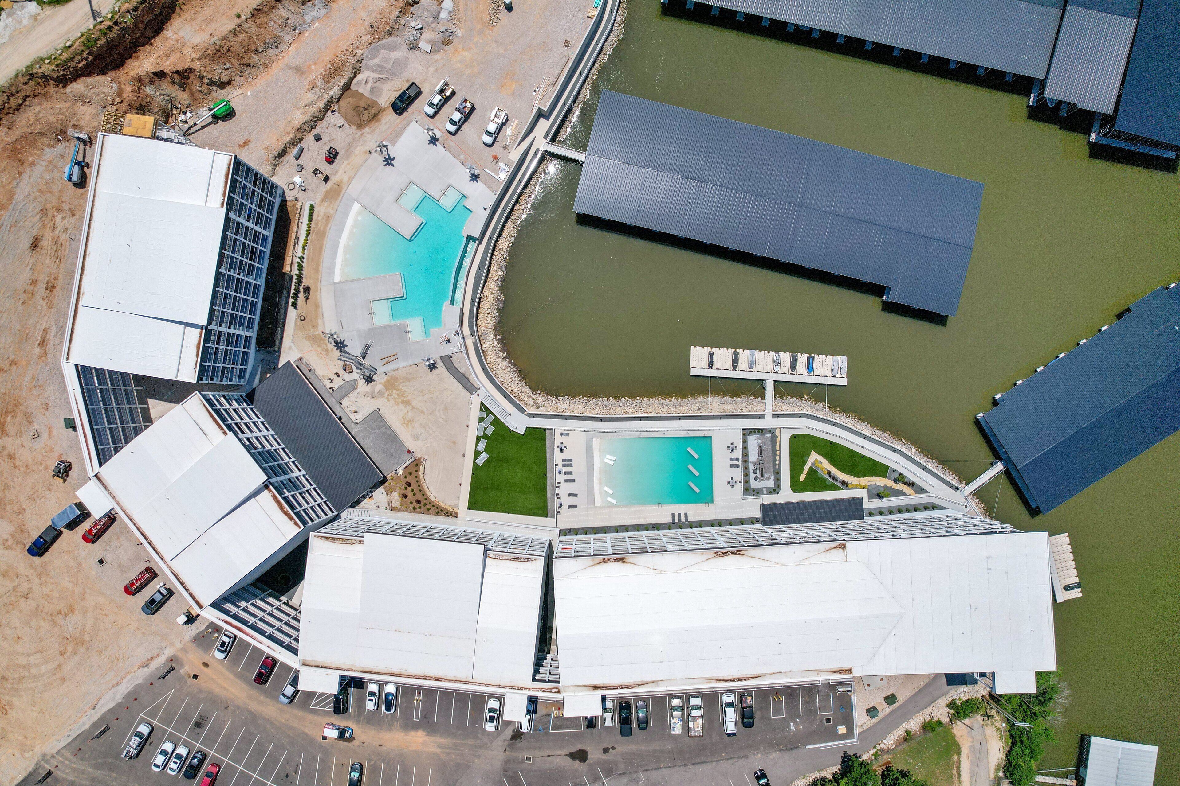 Vista aérea de un edificio moderno con piscina, estacionamiento y un cuerpo de agua cercano.