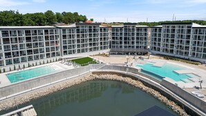 Un hotel moderno con varios pisos, una piscina central y una zona ajardinada con sillones de descanso.