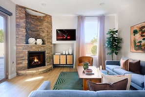 A modern living room with a stone fireplace, a flat-screen TV, a dining area, and a large plant. - Citrus-Pool & Spa-Walk 2 restaurants, shops & bars (Phoenix)