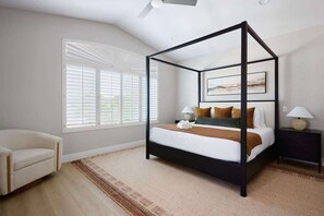 Un dormitorio con cama con dosel, una silla, una mesita de noche y una ventana con persianas.