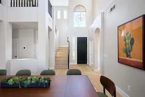 Un comedor con una mesa larga, sillas, un centro de mesa con planta, una escalera y una puerta.