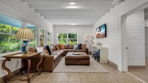 Un salon spacieux avec un grand canapé d’angle, une table basse et une lampe. Une fenêtre offre une vue sur la verdure environnante.