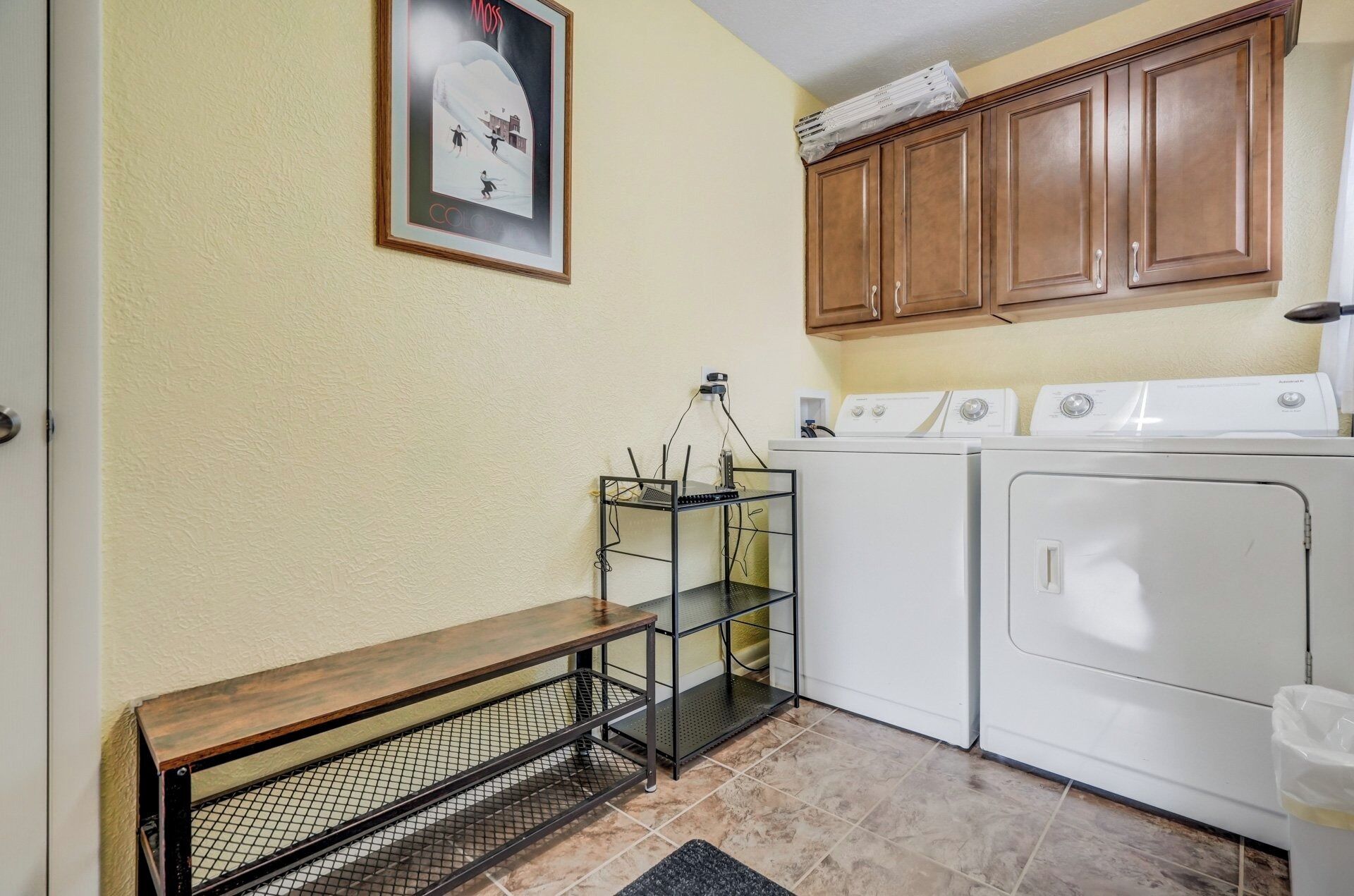 A laundry room with a washing machine, dryer, and a metal rack with a wooden bench.