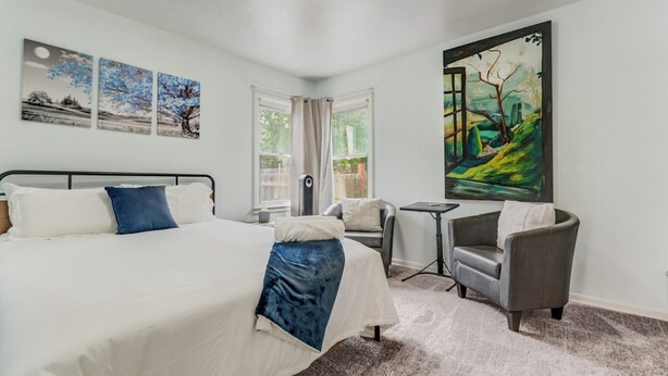 Een slaapkamer met een bed, twee stoelen, een klein tafeltje en kunstwerken aan de wanden.