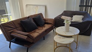 Un salon moderne avec un canapé en cuir marron, un petit divan et une table ronde agrémentée d’un vase de fleurs.