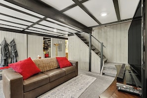 A living room with a brown leather sofa, red cushions, a patterned rug, a staircase, and a fireplace. - Harbor Springs, walking distance, base of Nubs two minutes to Highlands+hot tub. (Harbor Springs)