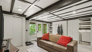 Una sala de estar moderna con un sofá de cuero, una mesa de centro de madera y una cocina visible a través de una puerta abierta.