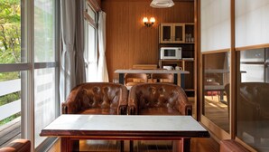 A dining area with two leather chairs, a wooden table, and a view of the outdoors through large windows. - rinne 2nd living Nasu Forest (Nasu)