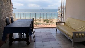 Ein Balkon mit Tisch und Stühlen, einer Couch und Blick auf das Meer sowie ein Schiff.