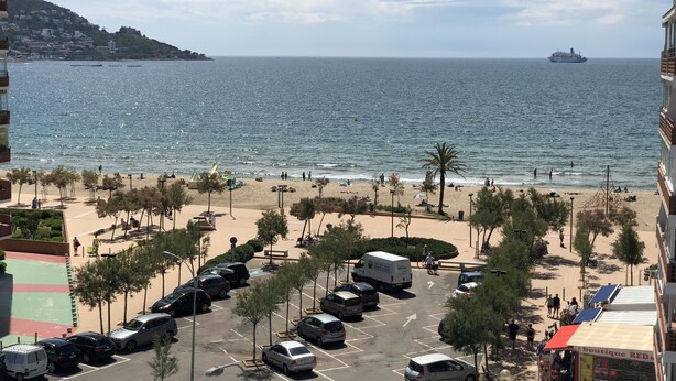 Eine Küstenstadt mit Strand, geparkten Autos und einem Schiffen am Horizont.
