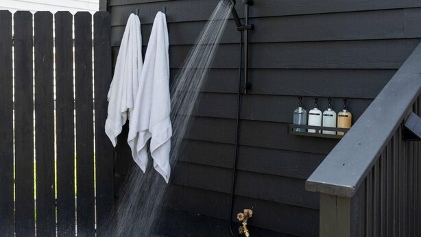 A showerhead with water flowing, a wooden fence, and a wall-mounted shelf with bottles.