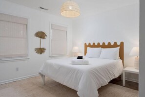 Une chambre à coucher avec un lit, des tables de chevet, un luminaire suspendu et une fenêtre avec des stores.