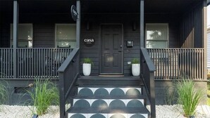 A dark-colored house with a front porch, a door labeled 'casa,' and two potted plants on the steps.