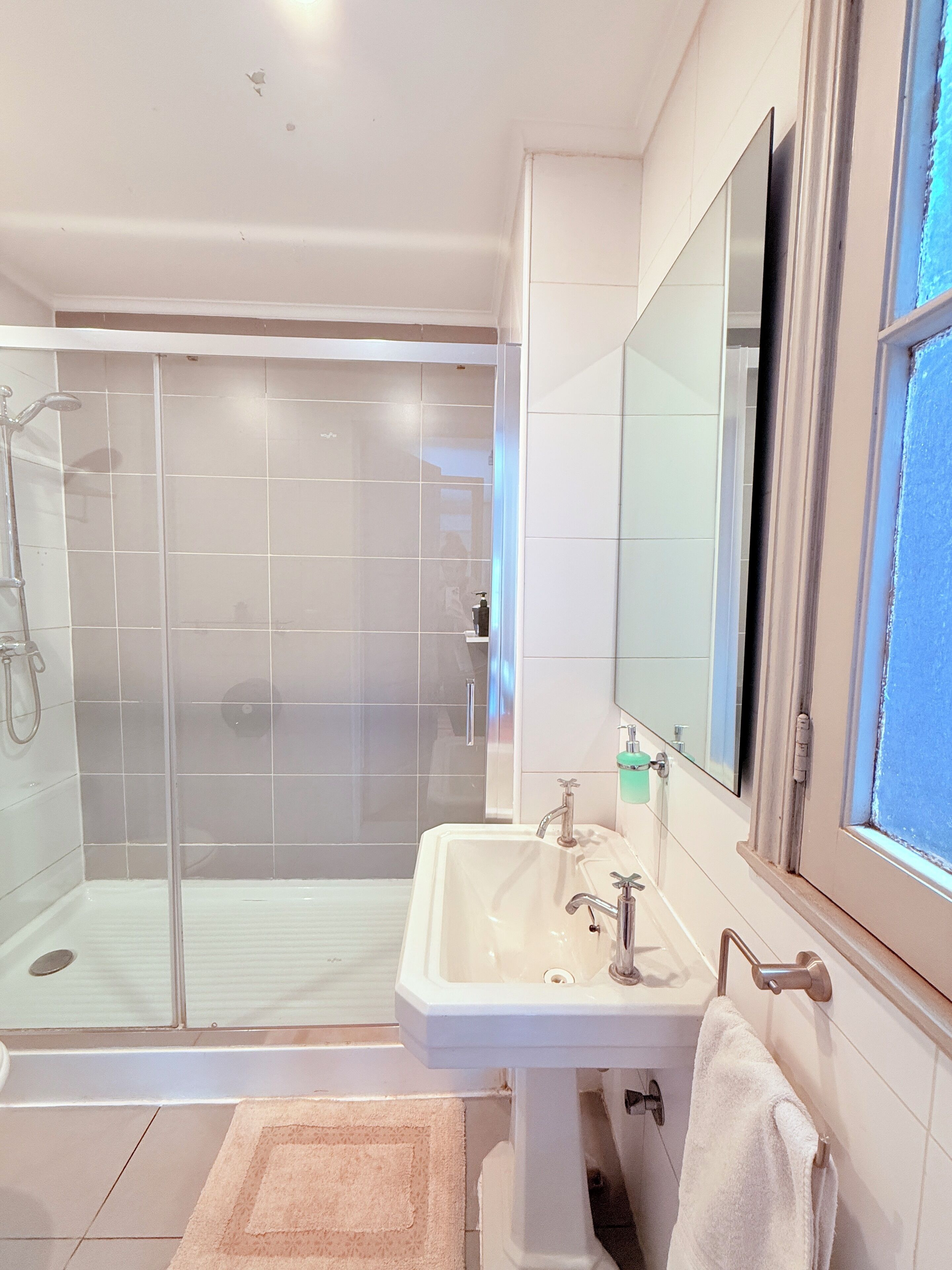 Un baño moderno con cabina de ducha de vidrio, un lavabo blanco con espejo y una toalla colgada en la pared.