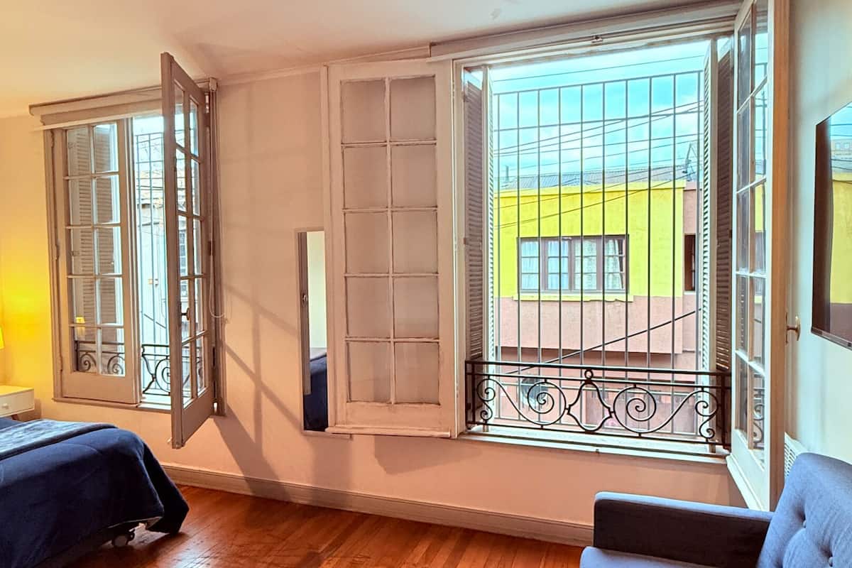 A hotel room with a bed, a chair, and a window with a view of a yellow building.