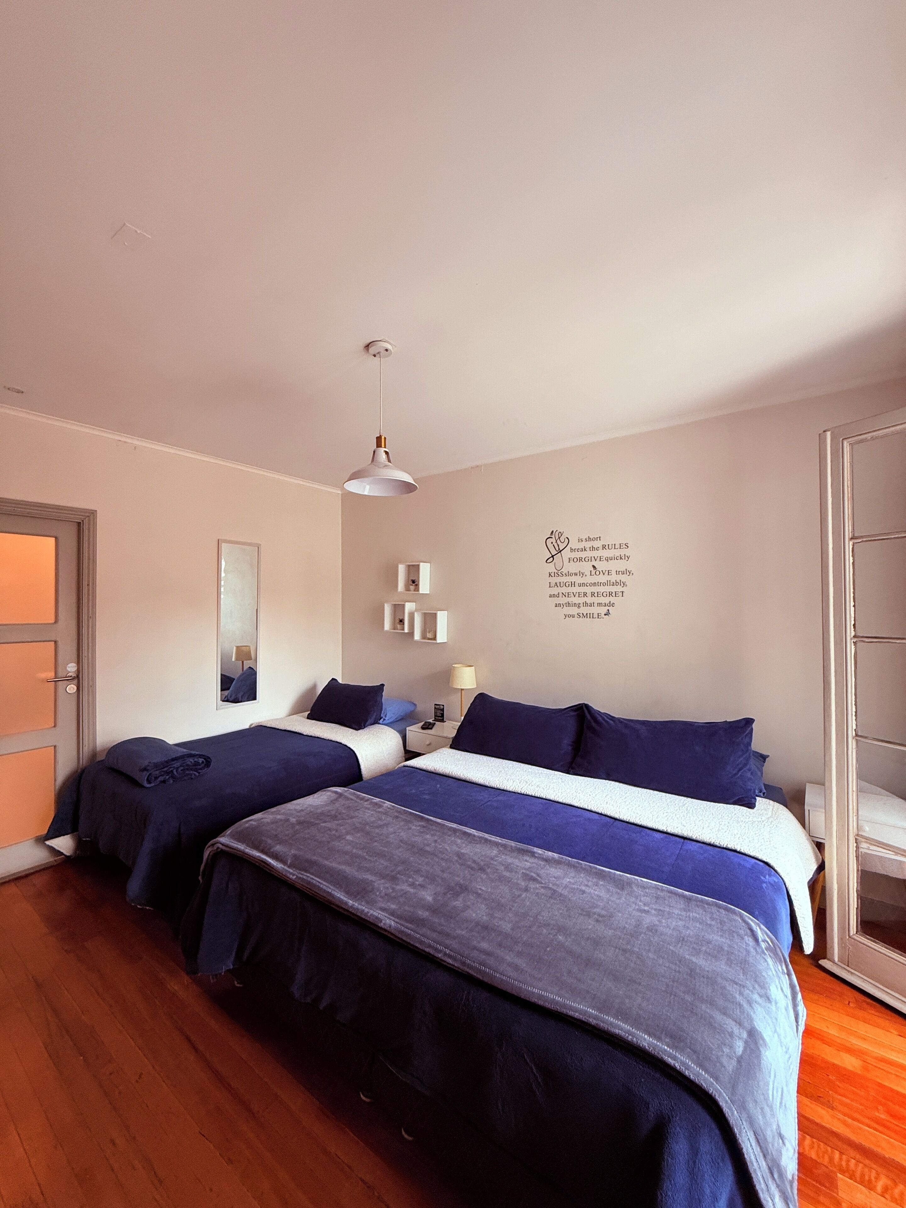 Hotelkamer met twee bedden, een spiegel, een wandlamp, een nachtkastje met een lamp, en een deur.