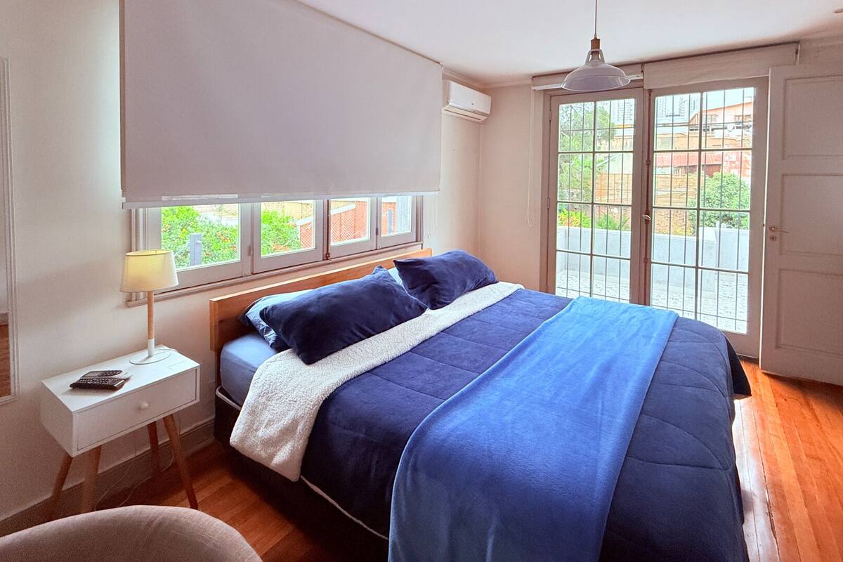 A bedroom with a bed, bedside table, lamp, and a view through a window.