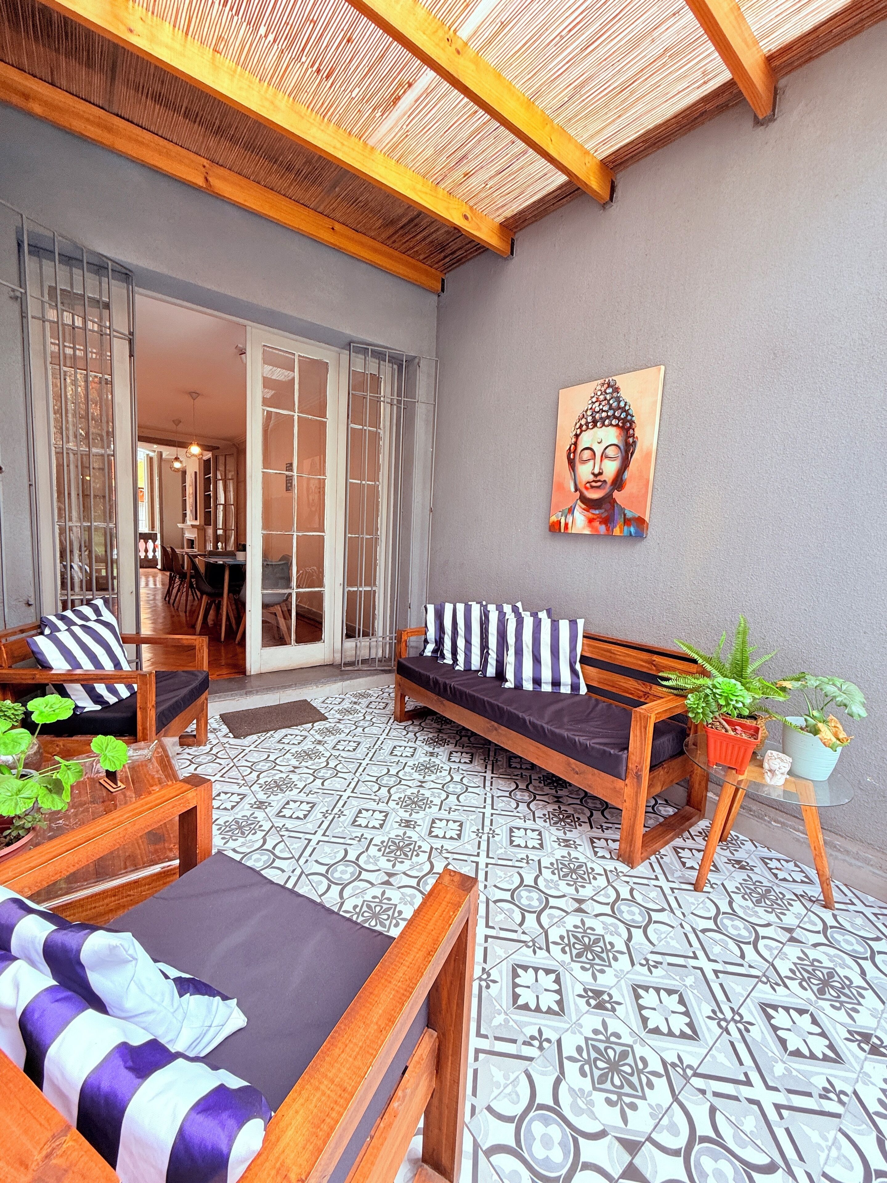 A cozy outdoor seating area with a wooden bench and sofa, a patterned floor, and a Buddha painting on the wall.