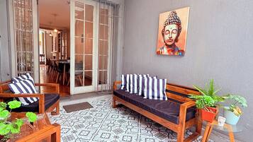 A cozy outdoor seating area with a wooden bench and sofa, a patterned floor, and a Buddha painting on the wall.