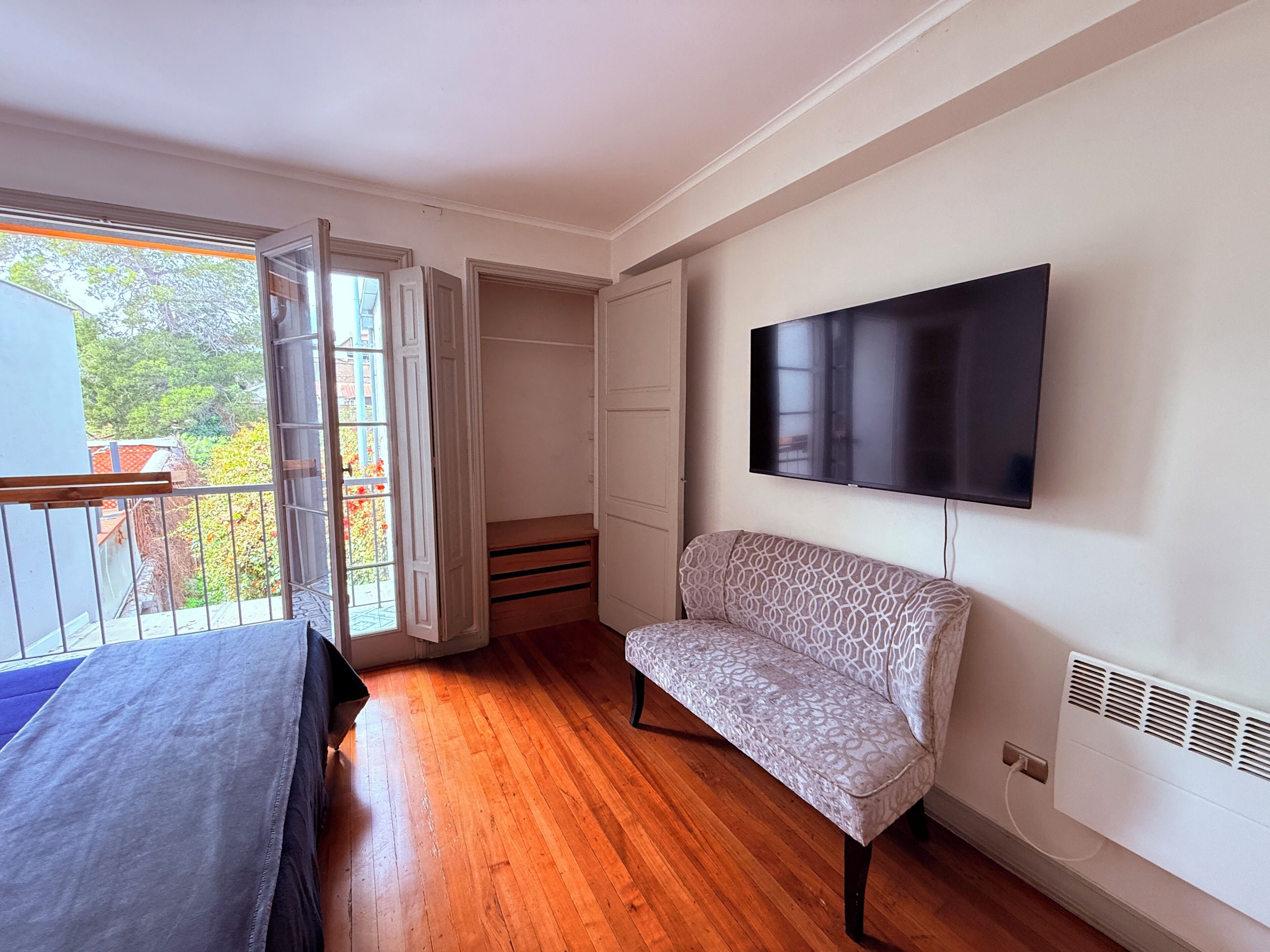 A room with a wooden floor, a sofa, a TV mounted on the wall, and a sliding door leading to an outdoor area.
