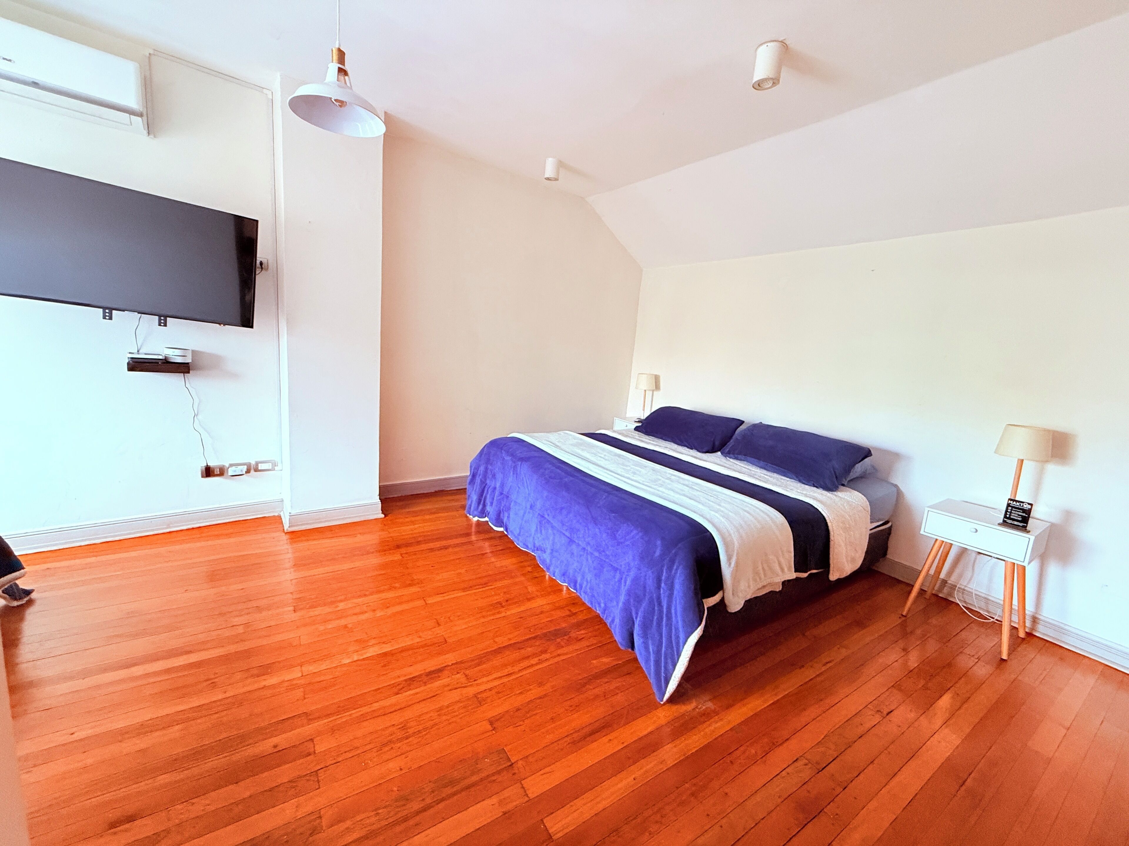 A bedroom with a bed, a TV mounted on the wall, and a wooden floor.