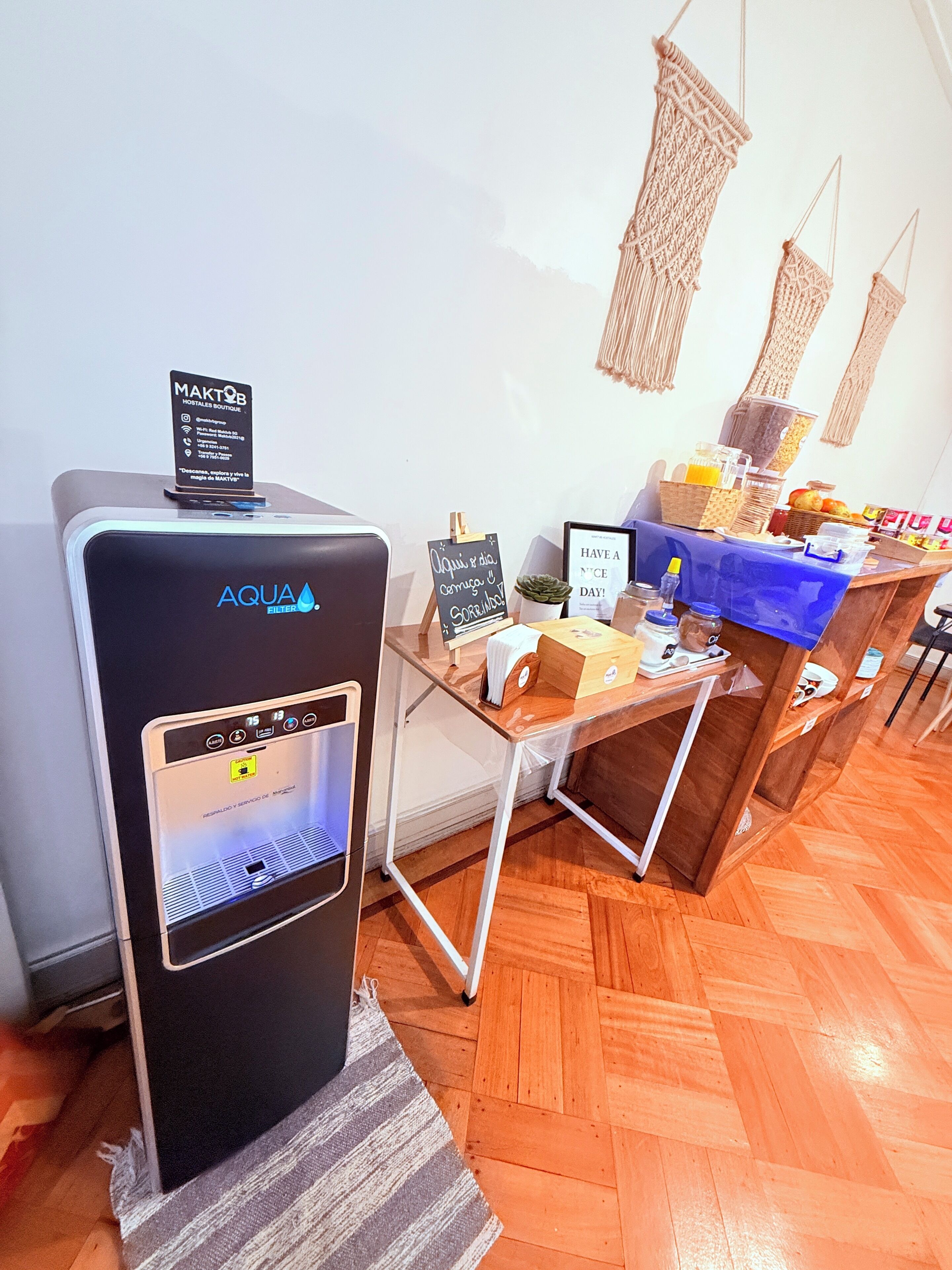 Una estación de filtrado de agua con pantalla digital, un cartel y una mesa con alimentos para el desayuno.
