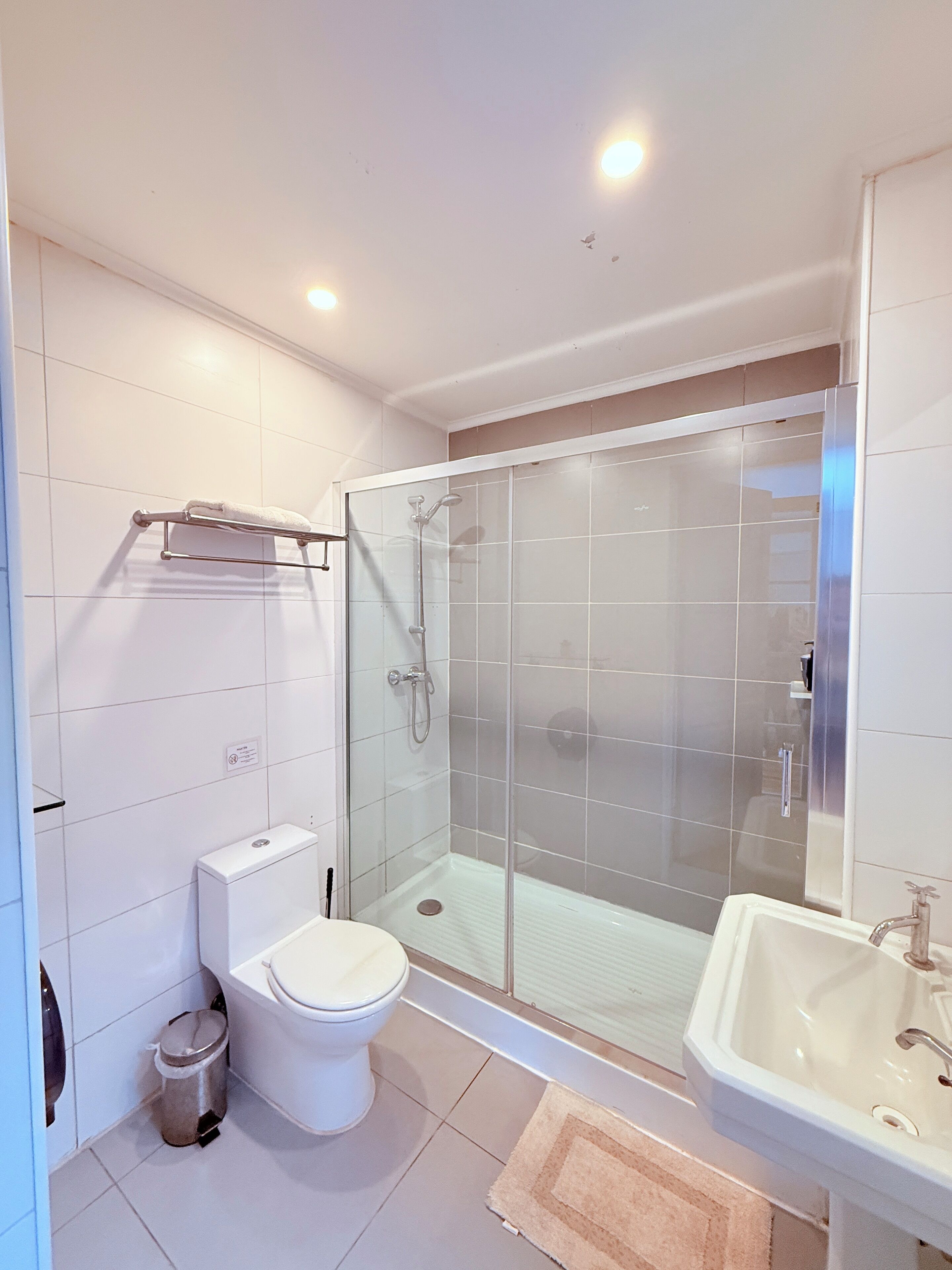 Un baño moderno con ducha envuelta en vidrio, inodoro, lavabo y toallero.