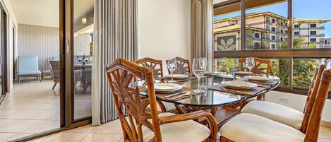 Un espace repas avec une table en verre, des chaises en osier et une vue sur les bâtiments à travers de grandes fenêtres.